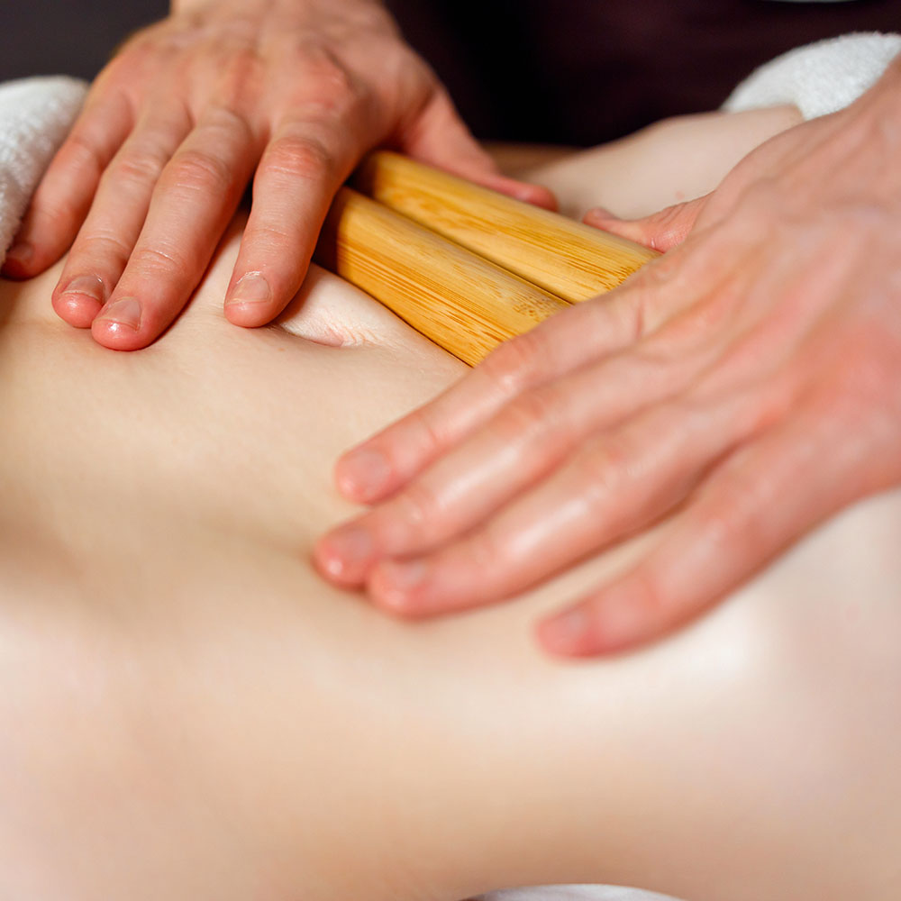 Massage therapist using two wooden bamboo sticks to massage stomach.